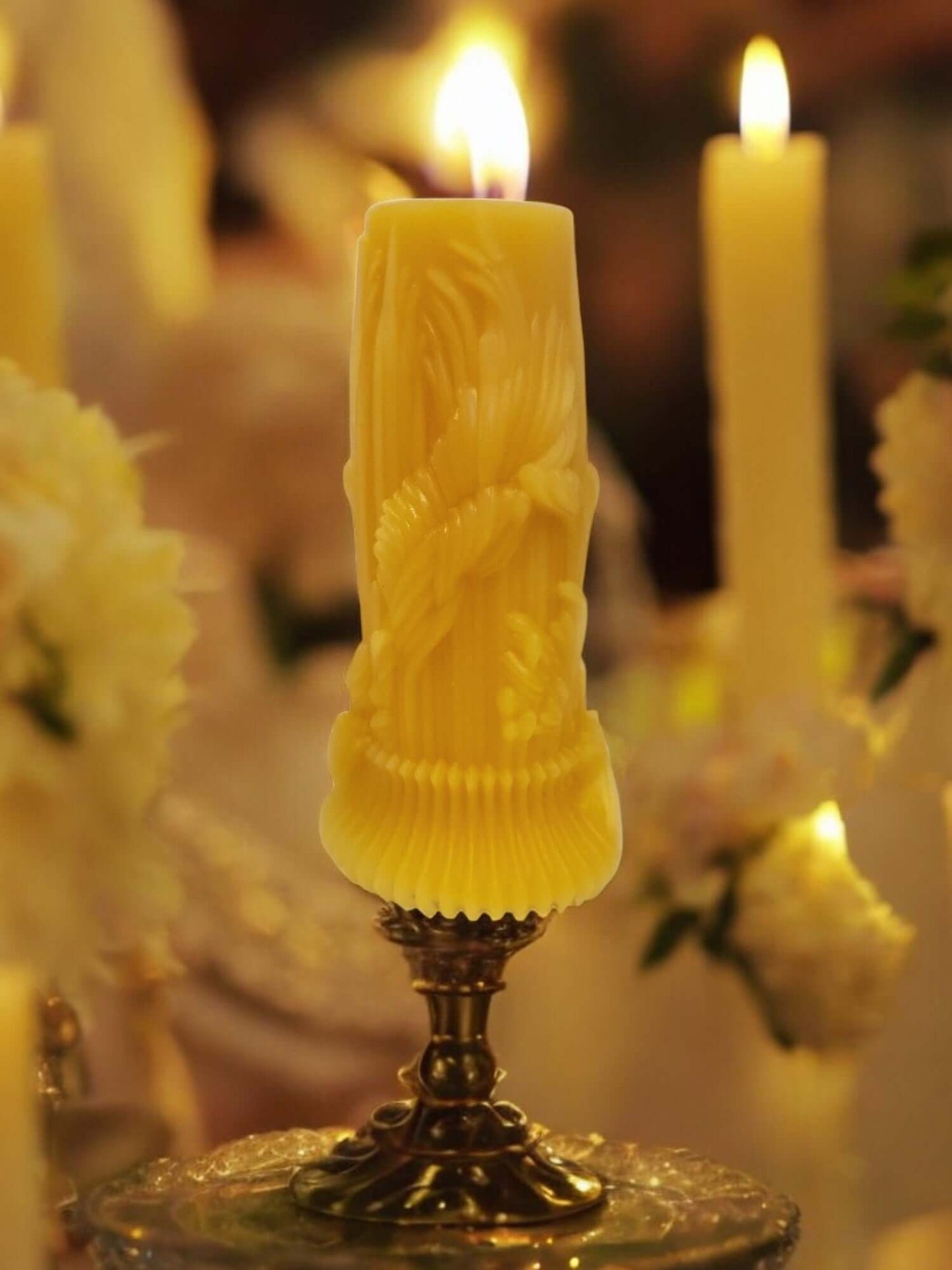Elegant yellow massage candle with intricate design, surrounded by white flowers and glowing candles.