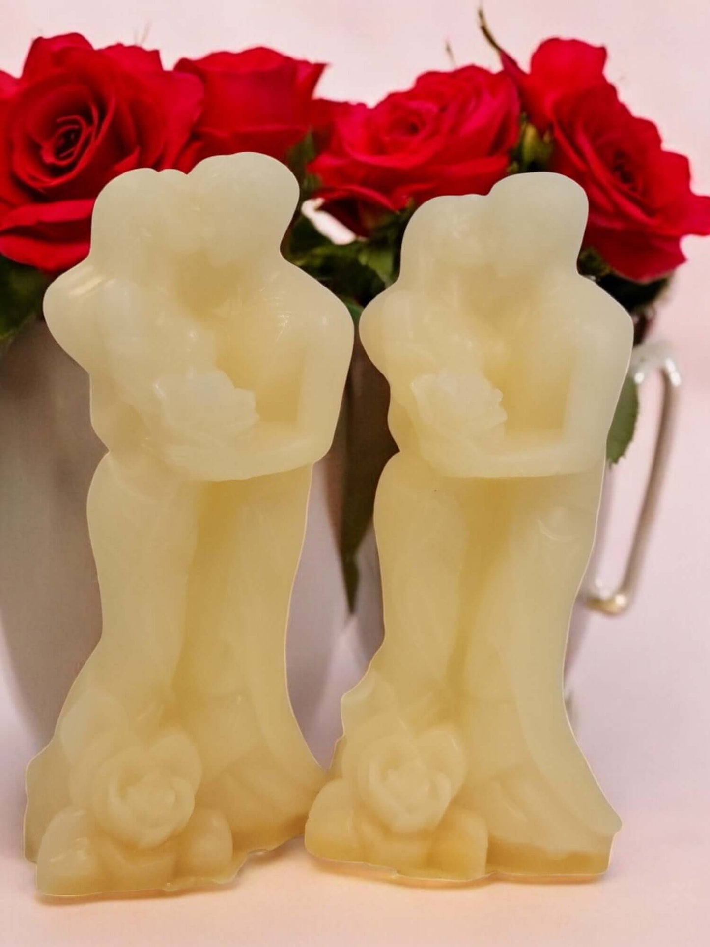 Couple-shaped massage candles in front of red roses, perfect for romantic and intimate experiences.