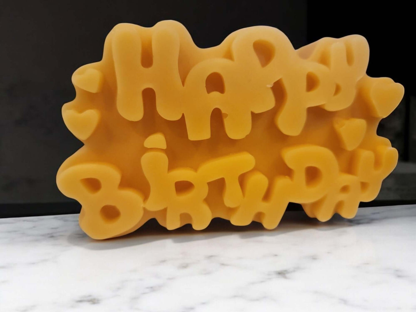 Happy Birthday candle with colorful letters on a marble surface, ideal for birthday celebrations and gifts.