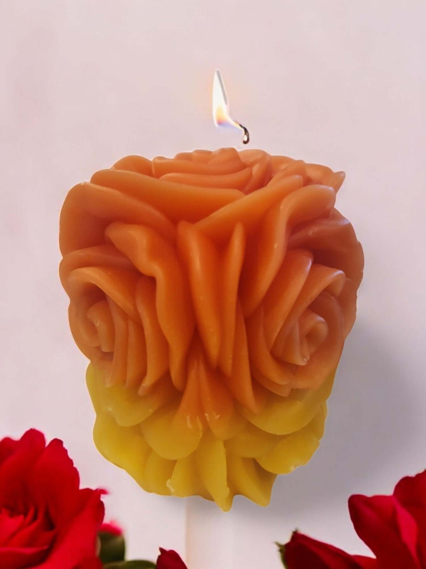 Rose-shaped massage candle melting for sensual play, with a warm glow and soft petals beside fresh roses.