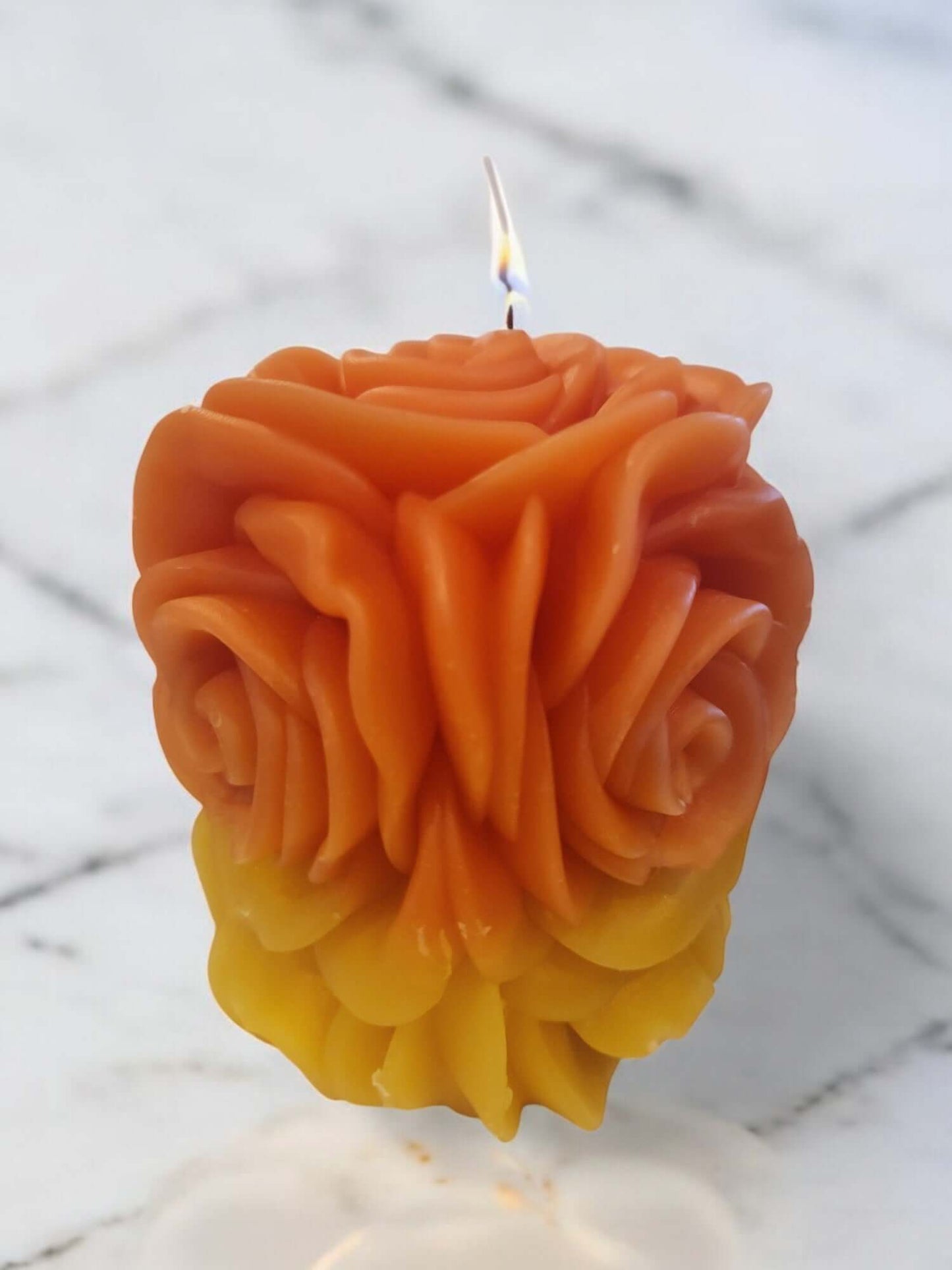 Sensual orange and yellow rose-shaped candle burning, perfect for massage and intimacy enhancement.