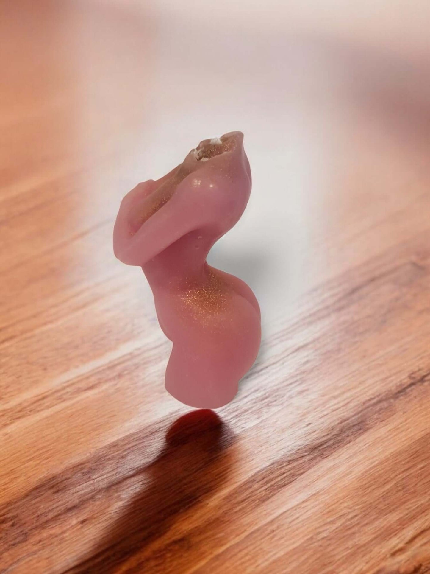 Stylized pink candle sculpture resembling a seductive figure on a wooden surface.