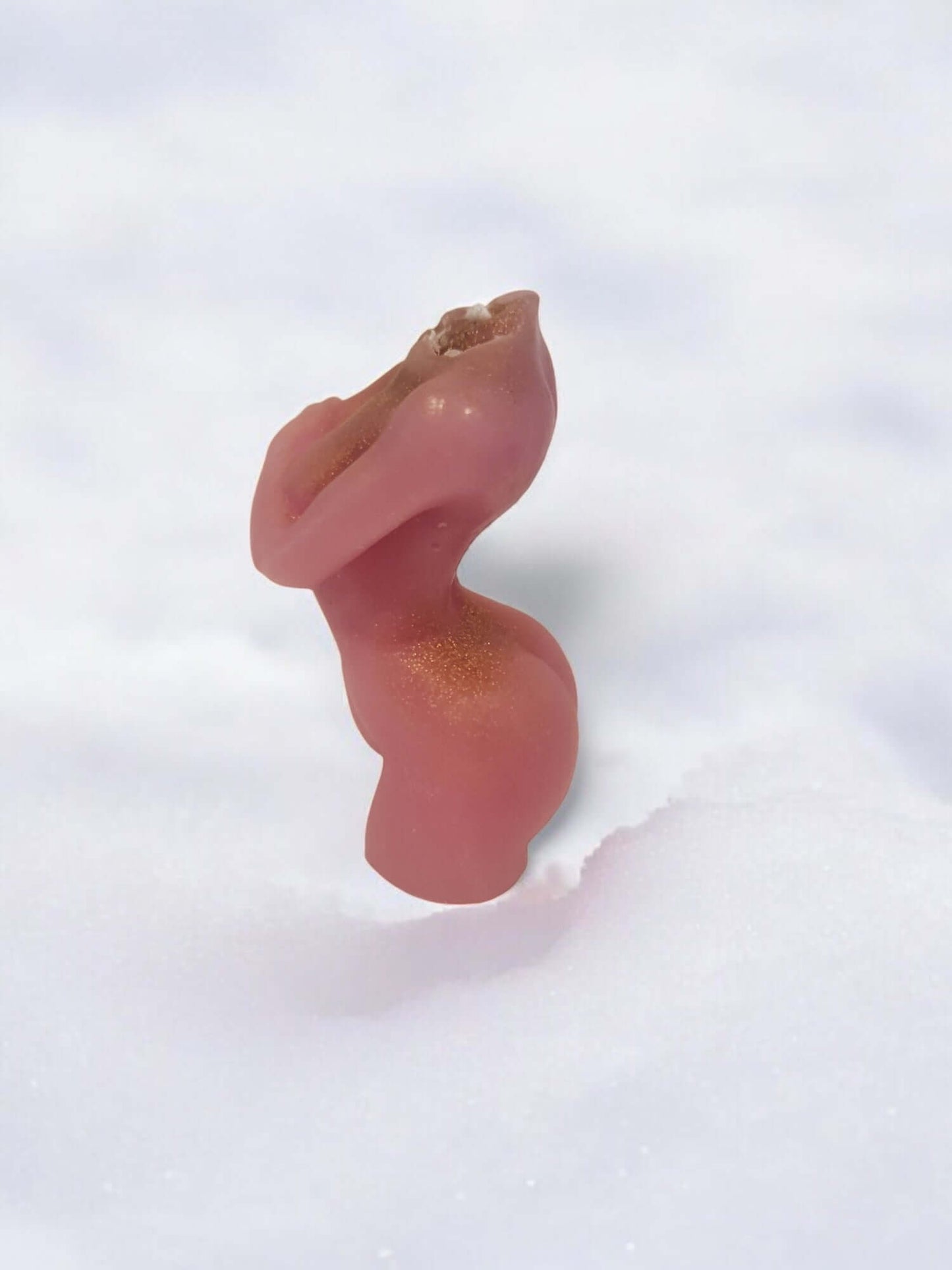 Artistic candle shaped like a curvy figure, standing in snow, emphasizing sensual design and intimacy.