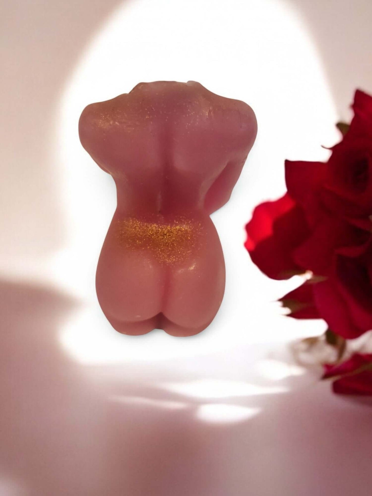 Sensual pink wax figure candle shaped like a torso, highlighted by red roses in the background.