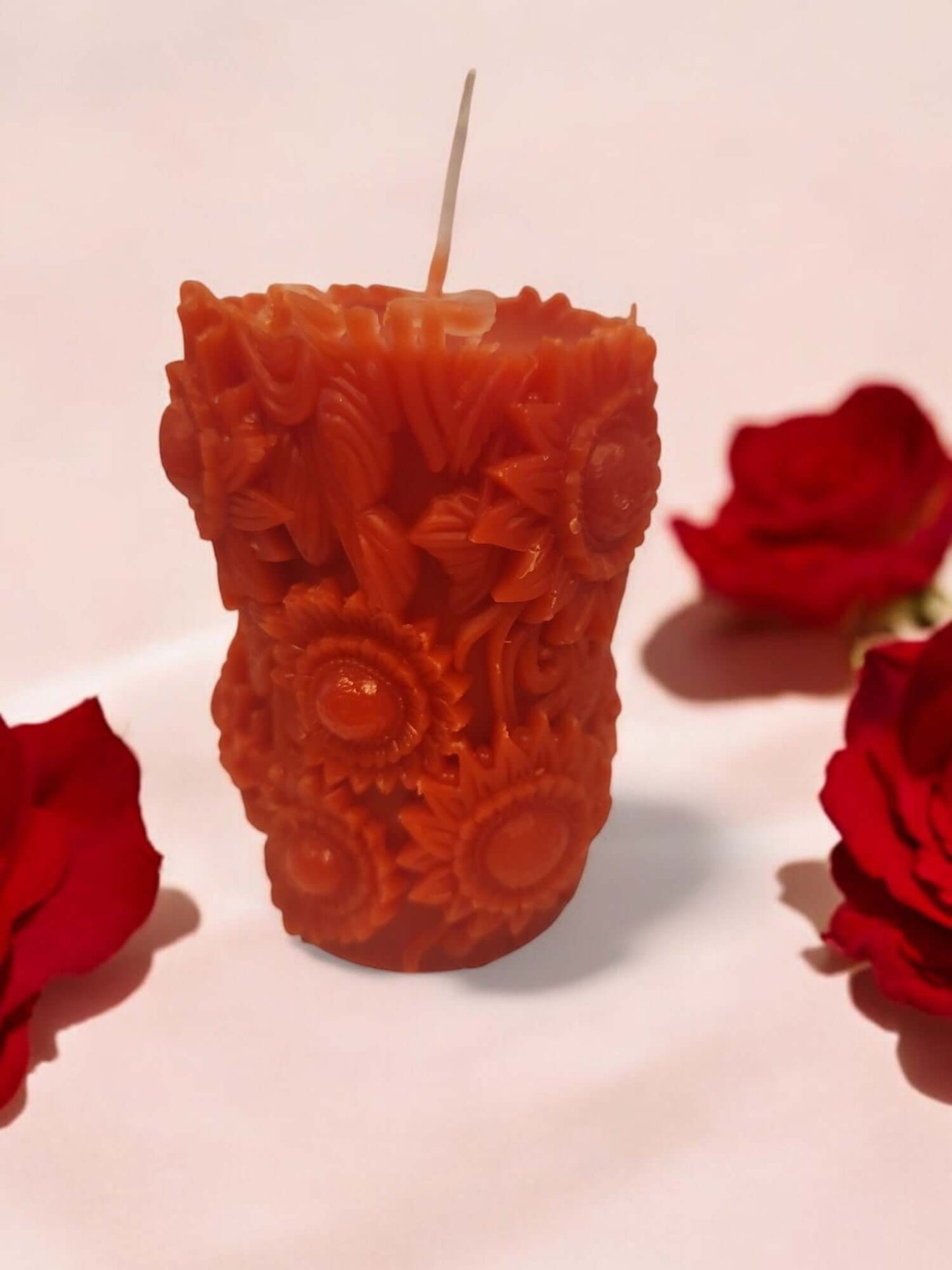 Sensual orange rose candle with floral design, surrounded by red roses, perfect for intimate moments and relaxing massages.