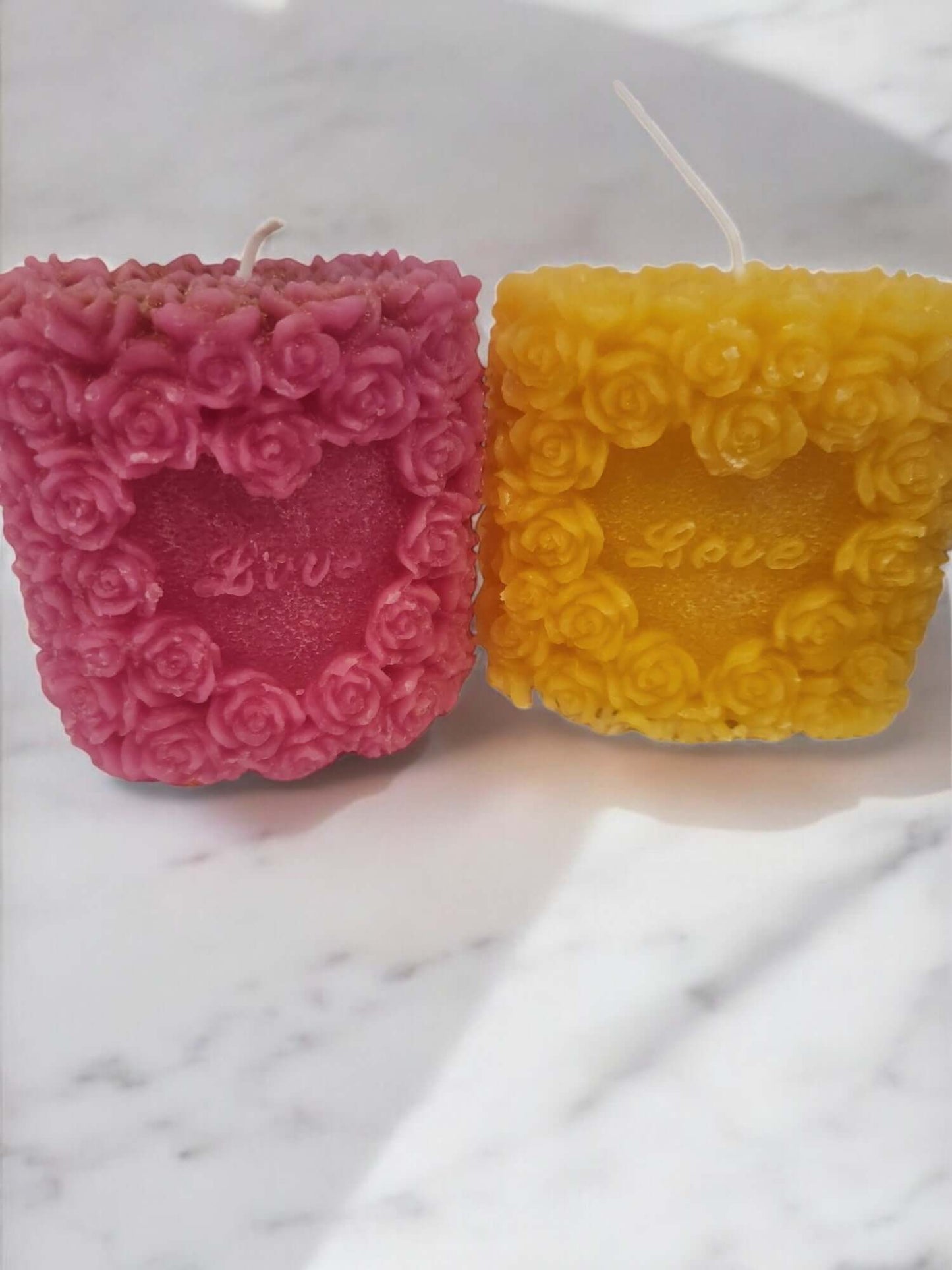 Two rose-shaped massage candles in pink and yellow, labeled 'Love,' for sensual and intimate experiences.