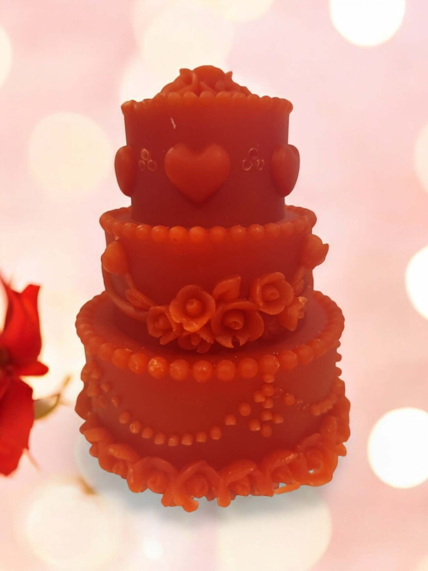 Elegant three-tiered orange candle shaped like a wedding cake, decorated with floral details and hearts.