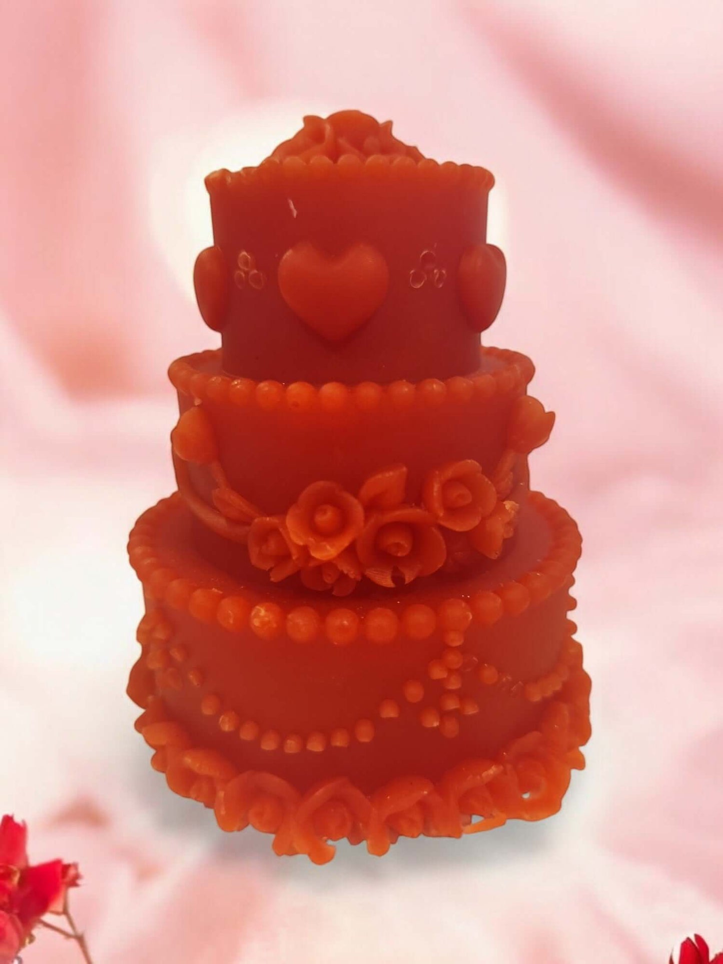 Beautifully crafted orange massage candle shaped like a wedding cake with decorative roses and hearts.