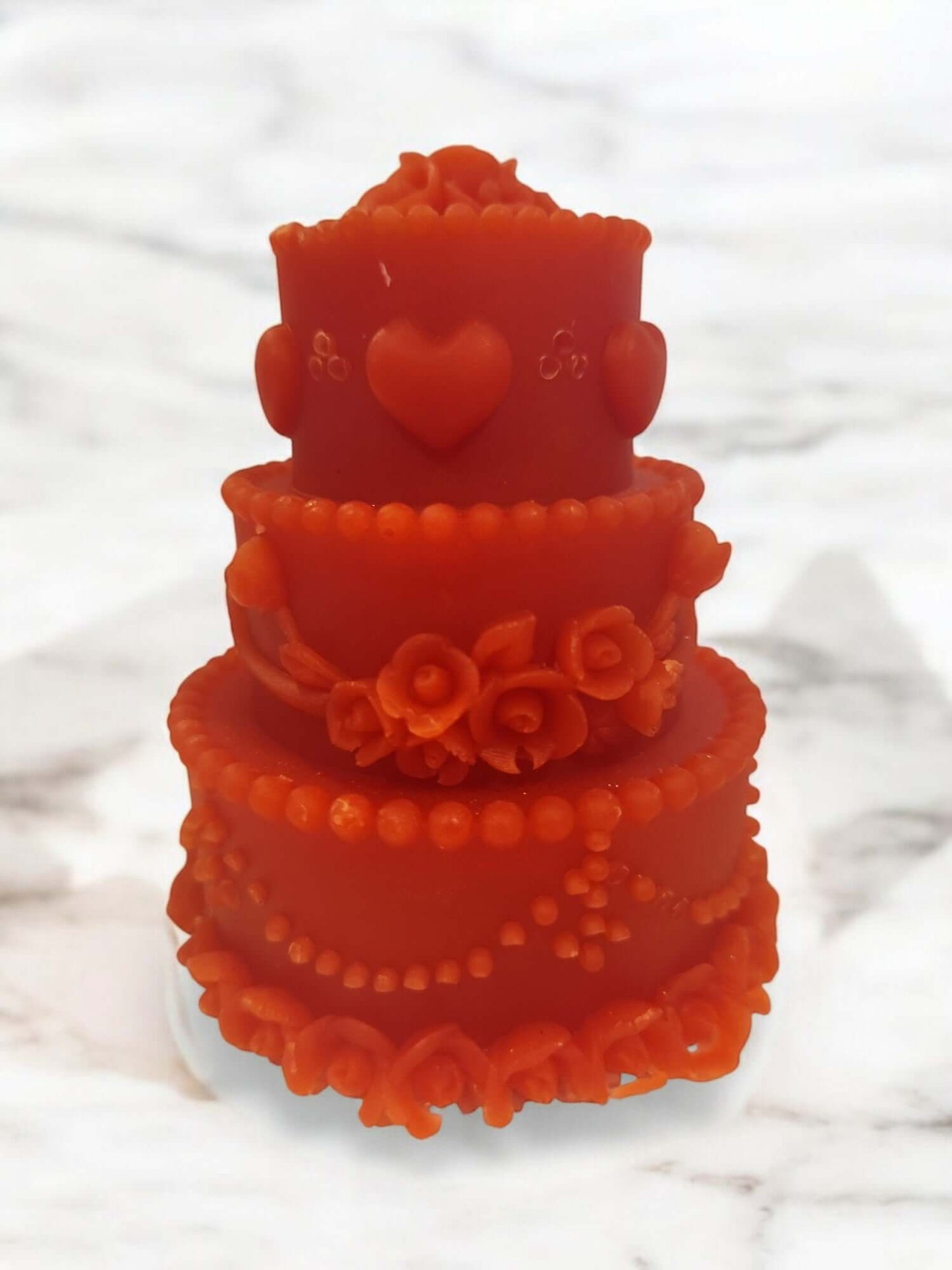 Orange romantic candle shaped like a three-tiered cake, adorned with roses and hearts, perfect for intimate moments.