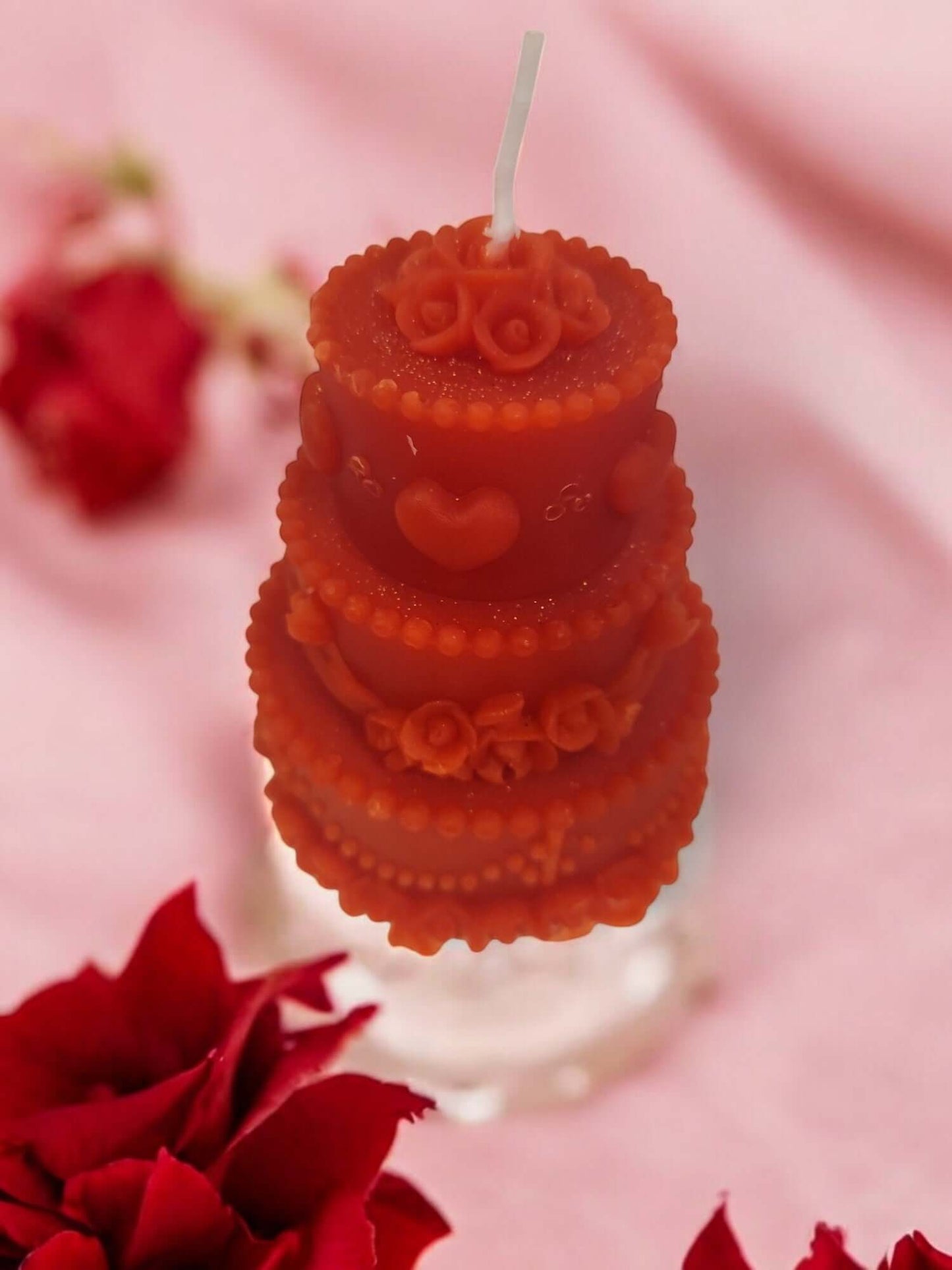 Sensual drip massage candle shaped like a cake, decorated with hearts, on a pink background with roses.