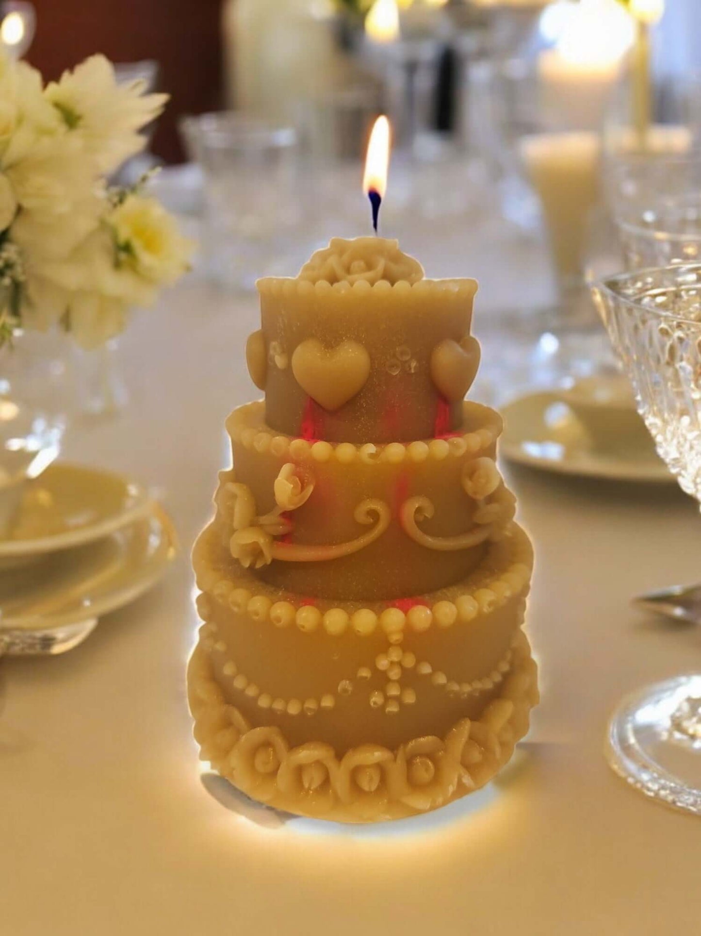Elegant wedding cake candle with decorative details and a lit flame, creating a romantic atmosphere for celebrations.