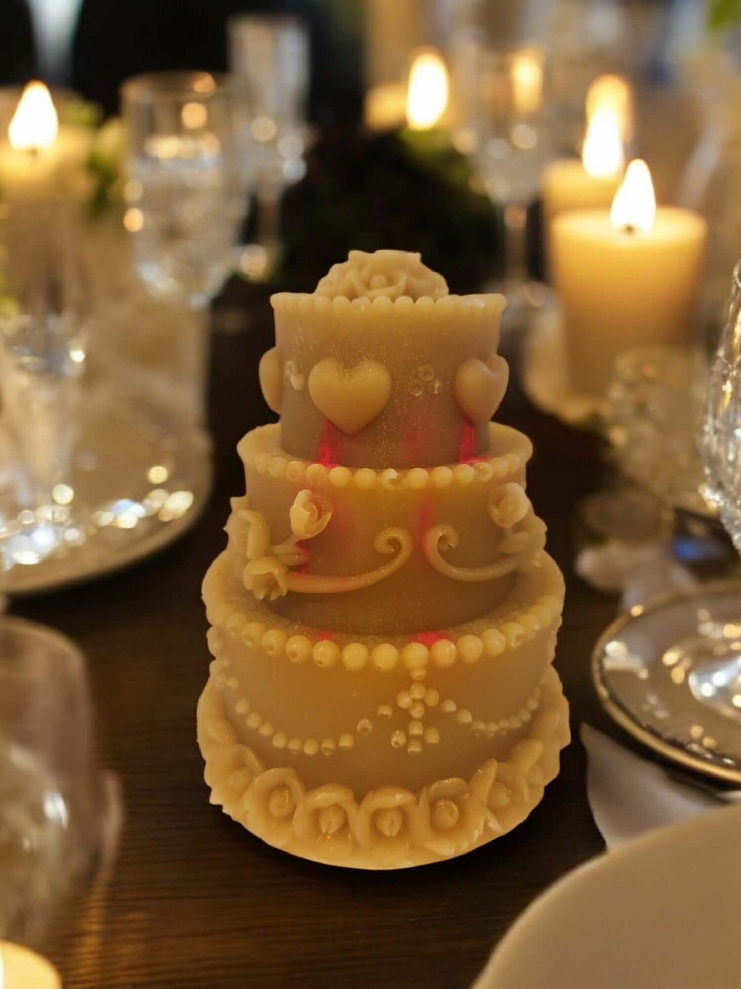 Elegant decorative candle shaped like a three-tier wedding cake, adorned with hearts and intricate frosting.