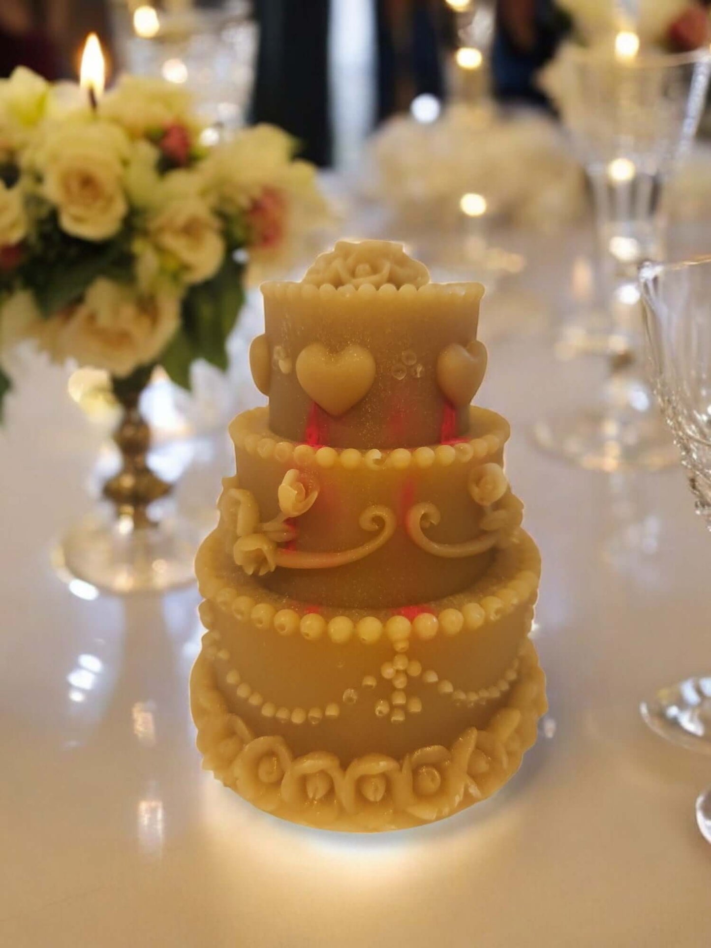Decorative tiered candle resembling a wedding cake, featuring hearts and floral details at an elegant table setting.
